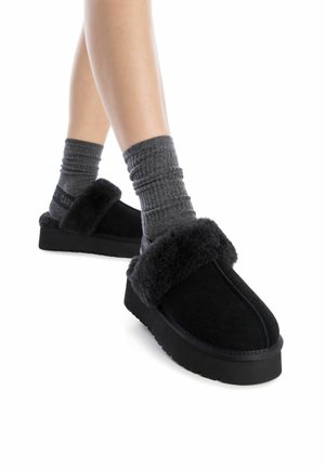 Zapatos negros sin cordones con un suave y esponjoso ribete y superficie texturizada. Suela de goma, material de ante, combinados con calcetines grises de canalé.