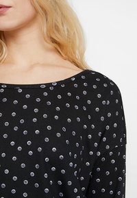 Schwarz langer Ärmel Oberteil mit weitem Ausschnitt und weißem Polka-Dot-Muster mit strukturierten Akzenten, aus einem weichen, gerippten Stoff gefertigt.