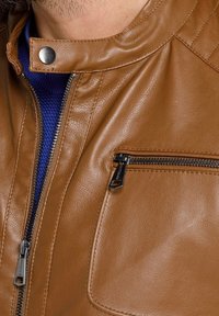 Giacca in pelle marrone con colletto a chiusura a scatto, cuciture orizzontali e tasca con zip sul lato sinistro. Texture liscia e design aderente.