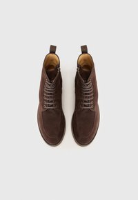 Stivaletti in suede marrone, con punta arrotondata, chiusura con lacci sul davanti e zip laterale, dotati di lacci marroni e fodera interna color beige.