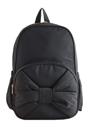 Fekete hátizsák elülső zsebbel, amely nagy párnázott masni alakú, dupla cipzáras záródással, fehér háttér előtt bemutatva.