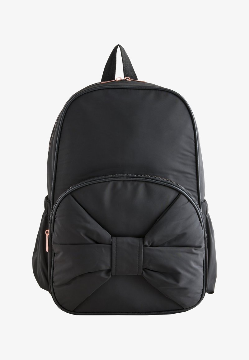 Sac à dos noir avec poche avant en forme d'un grand nœud rembourré et fermetures éclair doubles, présenté sur fond blanc.