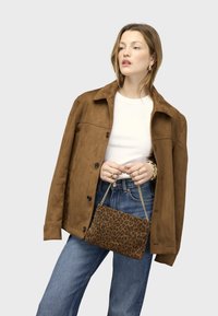 Hnědá semišová bunda přes bílý top, doplněná modrými džíny. Drží leopardí kabelku se zlatým řetízkovým popruhem.