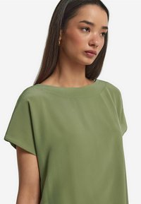 Grön kortärmad topp med en vid båtformad halsringning, tillverkad av ett slätt tyg, med en avslappnad passform och en minimalistisk design.