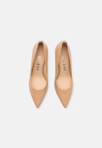 Nude leather pointed-toe pumps with smooth texture and slightly raised heel; interior features embossed branding "GUESS."