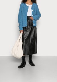 Světle modrý pletený cardigan s velkými knoflíky, bílý tričko, černá kožená midi sukně a černé boty na podpatku. Béžová kabelka přes rameno.