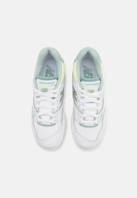 Zapatillas de cuero blancas con acentos en verde y amarillo, que presentan un diseño de cordones, cuello acolchado y branding grabado en los lados y en la lengüeta.