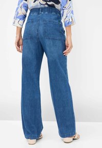 Wide-leg blue denim jeans with a high waistband, featuring two back pockets and a clean hem. Smooth texture and consistent color throughout.