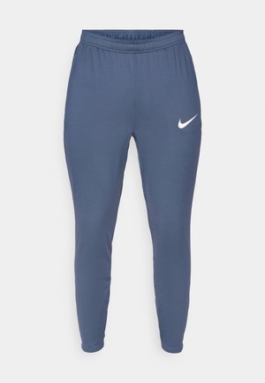 Nike dressipüksid tumesinisest kangast, millel on elastne vöökoht, kitsenevad sääred ja valge logo vasakul reitel. Pehme ja sile tekstuur.