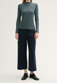 Maglia a maniche lunghe con collo alto, caratterizzata da un motivo a strisce orizzontali teal e bianche; abbinata a pantaloni a gamba larga blu navy e scarpe nere.