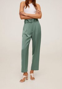 Pantalon taille haute plissé en tissu vert menthe avec une large ceinture. Associé à des sandales à talons blocs beiges et un débardeur blanc côtelé.