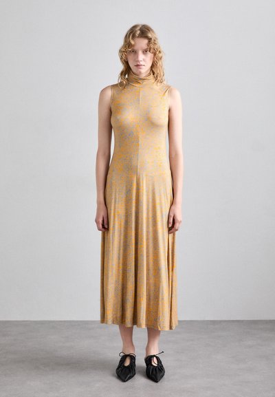 Lichtgele jurk met een abstract oranje patroon, mouwloos, hoge hals, A-lijn silhouet, tot midden kuit reikend, gecombineerd met zwarte schoenen.