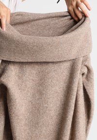Pull beige en maille avec un col large côtelé et un tissu doux et texturé. Le modèle présente une coupe ample décontractée et une sensation de confort.