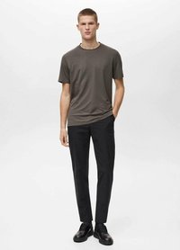 Tmavě šedé tričko s krátkým rukávem, jednoduchý design, spárované s černými slim-fit kalhotami a černými botami, stojící před jednobarevným pozadím.
