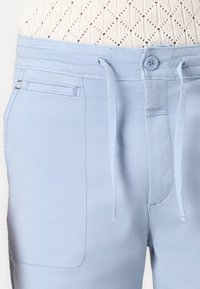 Shorts bleu clair en tissu doux, dotés d'une taille à cordon de serrage, d'une fermeture à bouton et de poches latérales avec des détails en couture.