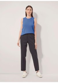 Blaues ärmelloses Top, kombiniert mit maßgeschneiderten schwarzen Hosen und weißen Sneakers. Das Outfit zeichnet sich durch ein elegantes Design und eine figurnahe Silhouette aus.