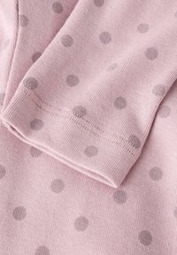 Lyserødt stof med en blød tekstur, der har grå polka dots i varierede størrelser og en syet kant på den foldede kant.