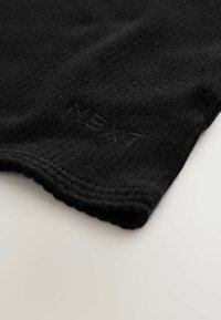 Černá pletená látka s jemnou texturou. Obsahuje volánkový lem a vystouplé logo "NEXT". Jednoduchý a minimalistický design.