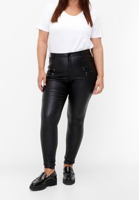 Svarta fusk läder skinny byxor med dragkedjefickor, matchade med en vit kortärmad skjorta och svarta loafers. Slät textur och figurnära design.