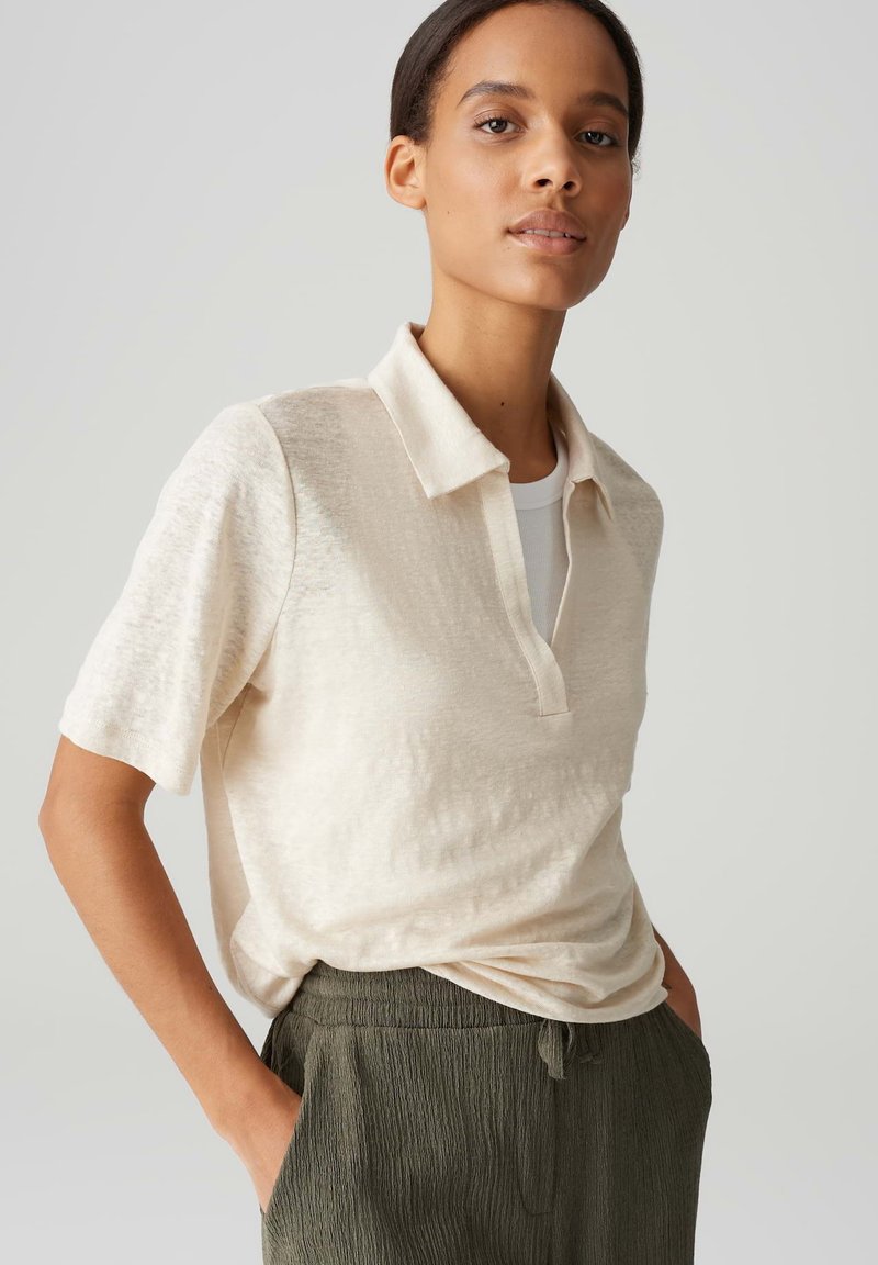 Polo shirt beige à manches courtes avec une coupe décontractée, doté d'un col et d'une texture subtile. Associé à un pantalon ample vert olive.