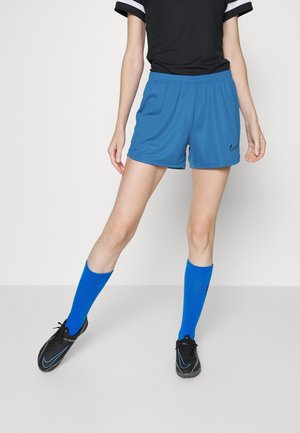 Shorts de sport bleus avec une taille élastique, associés à des chaussettes bleues montantes et des baskets noires avec un logo swoosh bleu.