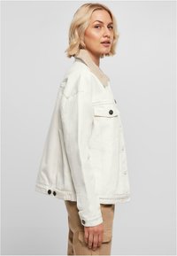 Veste en denim blanche avec un col en fausse fourrure beige, fermeture par boutons à l'avant, deux poches latérales et poignets à boutons.