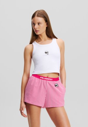 White ribbed tank top with a small black logo positioned at the center; paired with pink striped shorts featuring logo waistband and pocket.