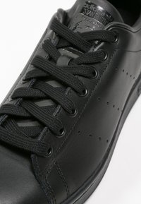 Sorte lædersneakers med en glat overflade, rund tå, klassisk snørebåndsdesign og perforeret detaljering på siden til ventilation.