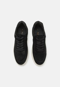 Fekete velúr sportcipők lapos fűzővel, kerek orral és fehér gumitalppal. A belső részen párnázott bélés található a kényelem érdekében.