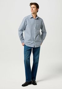 Camicia con bottoni in un motivo a scacchi blu e bianco, maniche lunghe e tasca sul petto, abbinata a jeans blu scuro e scarpe di pelle nere.