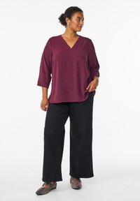 Haut prune à col en V avec des manches trois-quarts, associé à un pantalon noir ample et des ballerines à imprimé léopard, mettant en avant une coupe décontractée et un tissu texturé.