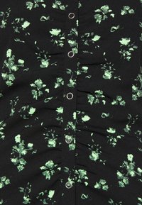 Czarna bluzka w kwiaty z zielonymi wzorami, funkcjonalnymi guzikami i marszczeniami dla uzyskania tekstury.