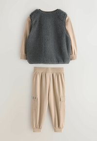 Dvoudílný outfit se šedou fleecovou vestou měkké textury a béžovými kalhotami s cargo kapsami a elastickými manžetami.