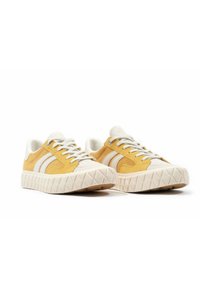 Gelbe Wildlederschuhe und weiße Textilsneaker mit einer geometrischen Gummisohle und drei weißen Streifen an den Seiten. Mit Schnürsenkeln. Flache Passform.