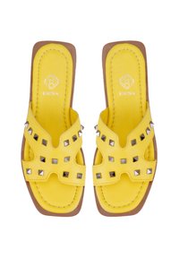 Gelbe Leder-Sandalen mit flacher Sohle, die mit einem Ausschnittdesign und metallischen Nieten verziert sind. Die Innensohle ist gepolstert für zusätzlichen Komfort.