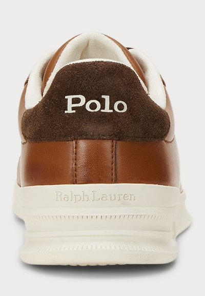 Rjavi usnjeni športni copati z belo gumijasto podplatom. Zadaj imajo temno rjavo nubuk usnje in belo "Polo" logo. Mehka obloga je vidna na ovratniku.