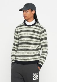 Gebreide trui in groen, marineblauw en wit met een horizontaal gestreept patroon; ribgebreide kraag en manchetten; model draagt een grijze pet en grijze broek.