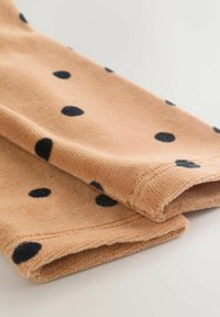 Pfirsichfarbener Fleece-Stoff mit großen schwarzen Punkten, der eine weiche Textur und sauber verarbeitete Kanten aufweist.