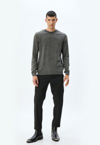 Grijze gestructureerde trui met lange mouwen, gecombineerd met slim-fit zwarte broek en zwarte chelsea boots, met een ronde halslijn.
