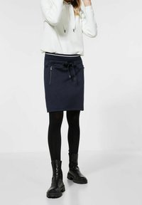 Mörkblå kjol i bomullsblandning med en åtsittande design, dragsko i midjan och två fickor med dragkedja. Bärs med svarta leggings och kraftiga svarta stövlar.