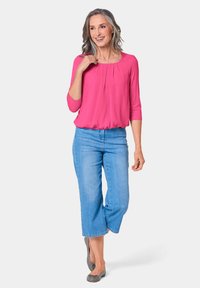 Fuchsia-Oberteil mit dreiviertel Ärmeln und Falten am Ausschnitt, kombiniert mit hellblauen, abgeschnittenen Jeans und grauen Ballerinas.