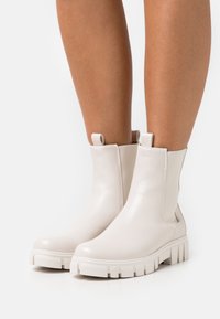 Białe skórzane botki do kostki z grubą podeszwą, elastycznymi bocznymi panelami oraz pętelkami. Gładka tekstura z połyskiem.
