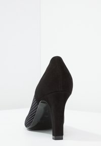 Zapato de tacón alto negro con un acabado de ante, tejido con un tejido de pied de poule texturizado en el lateral y puntera afilada.