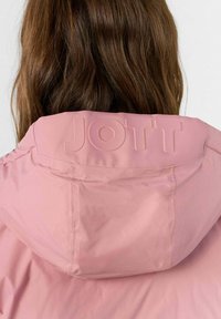 Giacca rosa con una texture liscia, presenta un logo "JOTT" in rilievo sulla parte posteriore del cappuccio, design leggero e senza hardware visibile.