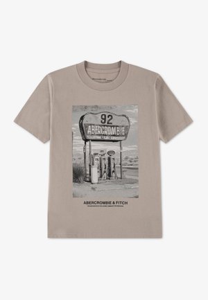 Beige t-shirt med vintage-stil sort-hvid tankstation tryk og "Abercrombie & Fitch" tekst under billedet.