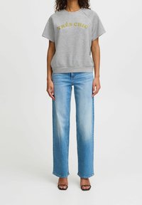 Grå sweatshirt med guldtryck "TRÈS CHIC", rund halsringning, korta ärmar, parat med ljusblå vida jeans och svarta klacksandaler.