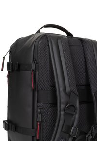 Mochila negra que presenta una combinación de materiales lisos y texturizados, correas de hombro acolchadas, detalles de malla y múltiples compartimentos con cremallera.