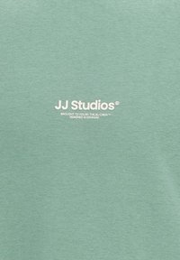 Tissu vert avec texte blanc centré indiquant « JJ Studios présenté par l'équipe J&J, conçu au Danemark »