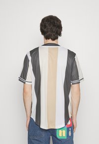 Camisa de manga corta con rayas verticales en beige, gris y blanco. Incluye acentos de rayas en contraste en las mangas.