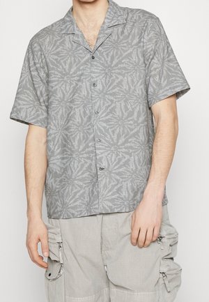 Uomo che indossa una camicia grigia a maniche corte con motivo astratto e pantaloni cargo grigio chiaro con più tasche.